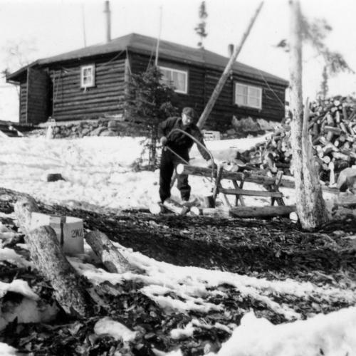 Man sawing wood at Negusville log cabin, 1940s (Arnold Smith Collection)