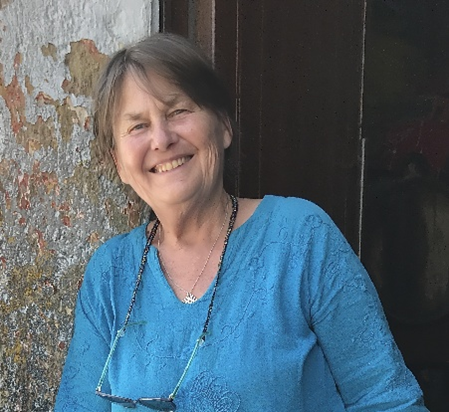 Fran Hurcomb, wearing a blue shirt and standing outside in front of a wall, smiling